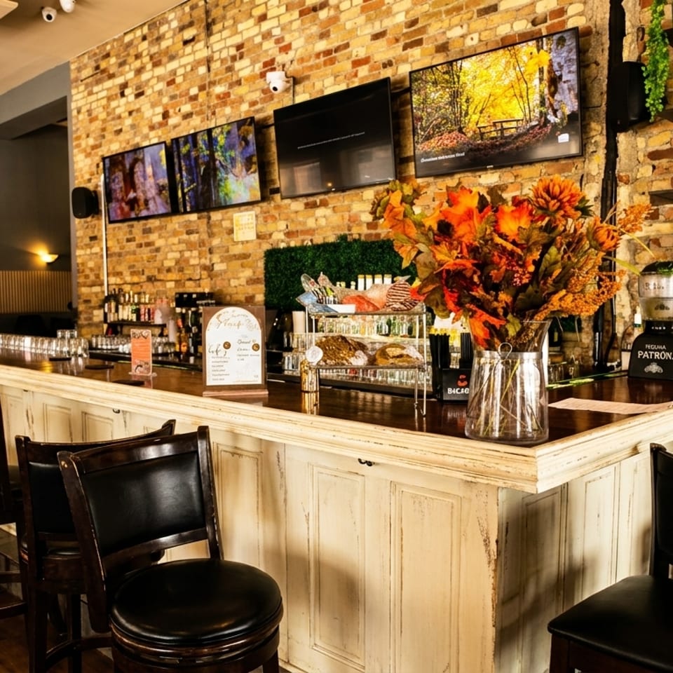 A cozy bar interior with brick walls, bar stools, and autumn decorations, featuring multiple screens.